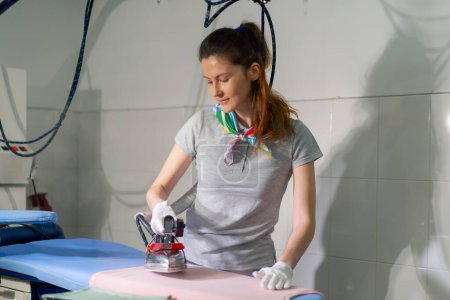 Téléchargez les photos : Nettoyage à sec professionnel jeune fille repassage rose avec fer professionnel à vapeur - en image libre de droit