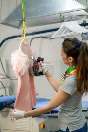 Photo for Professional dry cleaning young girl irons a pink sweater on a hanger with steam - Royalty Free Image