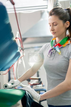 Photo for Professional dry cleaner a young girl uses an adhesive roller to remove wool on a black jacket using a press machine - Royalty Free Image