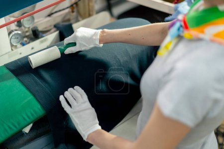 Photo for Top shot close up professional dry cleaner a young girl uses an adhesive roller to remove wool on a black jacket - Royalty Free Image