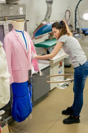 Photo for Professional dry cleaner a young girl takes a suit out of the dryer for finishing by hand press - Royalty Free Image