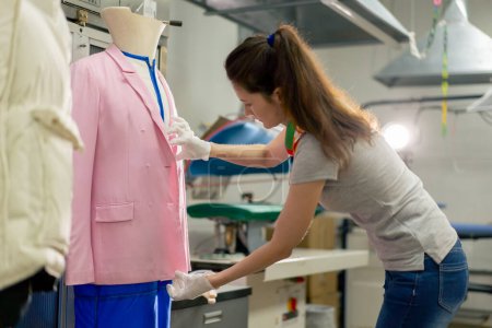 Photo for Professional dry cleaner a young girl takes a suit out of the dryer for finishing by hand press - Royalty Free Image