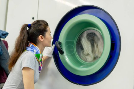 Téléchargez les photos : Professional dry cleaner, a young girl watches the washing process of a professional machine - en image libre de droit