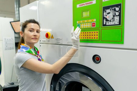 Photo for Professional dry cleaner young girl looking at the camera and posing near a professional washing machine - Royalty Free Image