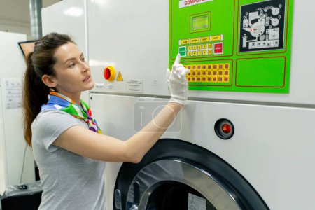 Photo for Professional dry cleaning young girl presses a button on the green panel of a professional washing machine - Royalty Free Image