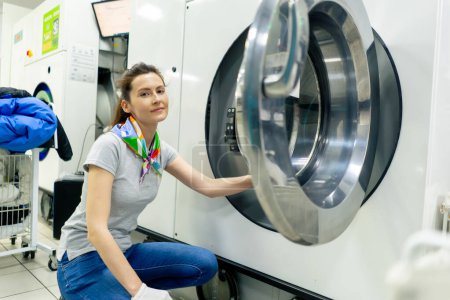 Téléchargez les photos : Professionnel nettoyage à sec jeune fille regardant la caméra et posant près d'une machine à laver professionnelle - en image libre de droit