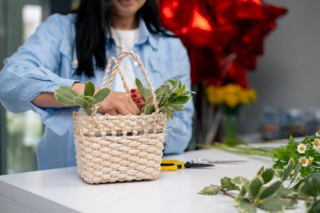 Photo for Close up in a flower shop a girl near a white table collects a flower arrangement a bouquet in a basket - Royalty Free Image
