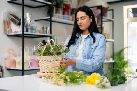 Photo for In a flower shop a girl near a white table collects a flower arrangement a bouquet in a basket - Royalty Free Image
