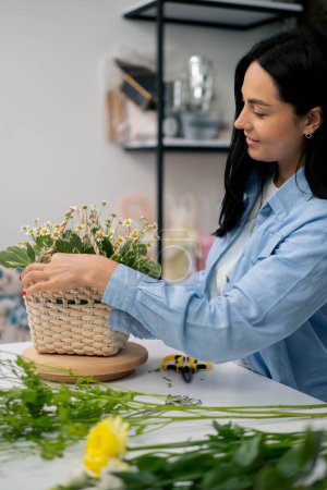 Photo for In a flower shop a girl near a white table collects a flower arrangement a bouquet in a basket - Royalty Free Image