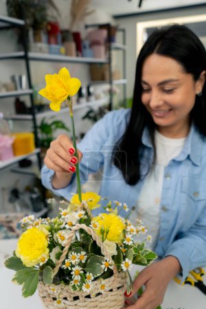 Photo for In a flower shop a girl near a white table collects a flower arrangement of yellow daffodils - Royalty Free Image