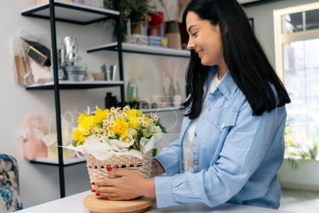 Photo for In a flower shop a florist admires a completed flower arrangement with yellow flowers in a basket - Royalty Free Image