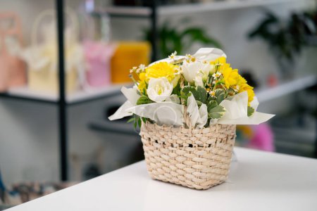 Photo for In flower shop on a white table there is a ready-made composition in a basket with a yellow bouquet - Royalty Free Image