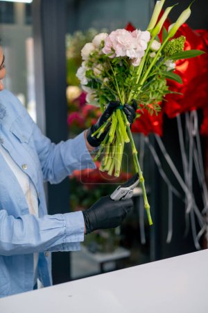 dans un magasin de fleurs une fille près d'une table blanche recueille un arrangement de fleurs et coupe les tiges