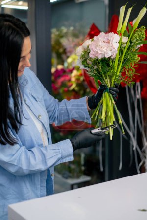in einem Blumenladen sammelt ein Mädchen in der Nähe eines weißen Tisches ein Blumengesteck und schneidet die Stängel