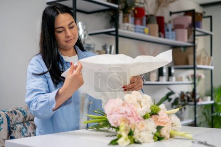 in a flower shop a florist prepares a white paper wrapper for decorating flowers flowers for a woman.