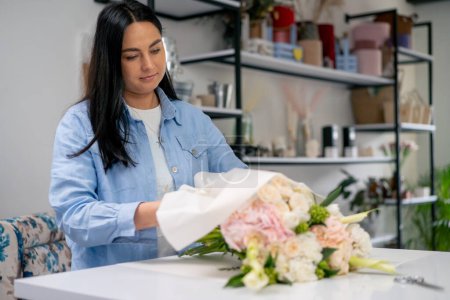 in a flower shop a florist wraps a ready-made delicate bouquet in a white paper wrapper