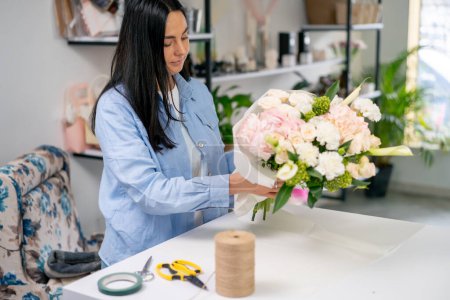 in a flower shop a florist wraps the finished tender in a white paper wrapper and ties it with a rope