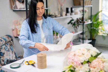in a flower shop a florist wraps a ready-made delicate bouquet in a white paper wrapper