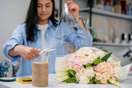 in a flower shop a florist wraps a ready-made tender in a white paper wrapper and cuts off a rope with a rope