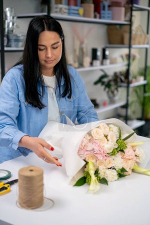 Photo for In a flower shop a florist wraps a ready-made delicate bouquet in a white paper wrapper - Royalty Free Image