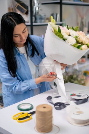 Photo for In a flower shop a florist ties a white ribbon to a completed flower arrangement - Royalty Free Image