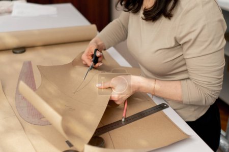 Photo for A professional seamstress works with craft paper to cut out future patterns for a dress - Royalty Free Image