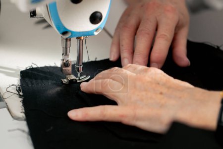Photo for Close up in a sewing workshop on a machine the seamstress master makes a cut on a black fabric - Royalty Free Image