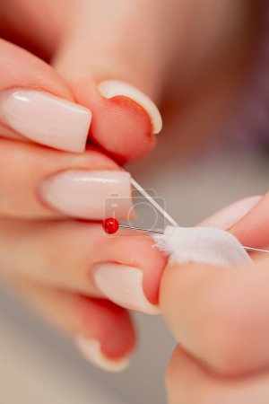 Photo for Close-up of hands in a sewing workshop hemming white fabric for a dress with a needle - Royalty Free Image
