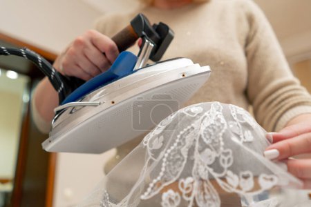 Photo for Close-up in a sewing workshop a woman irons a lace veil for the bride with a professional iron - Royalty Free Image