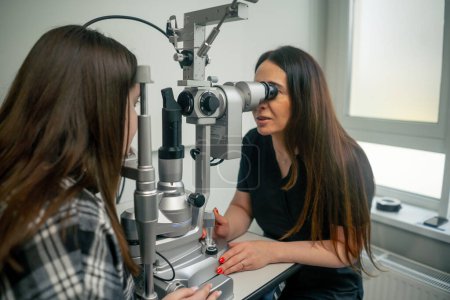 Téléchargez les photos : Dans une clinique d'ophtalmologie jeune médecin diagnostique une jeune fille avec une loupe - en image libre de droit