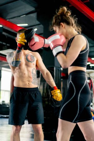 in a boxing fight club young girl in a black sweatshirt with pink gloves practices with a trainer close combat punch training