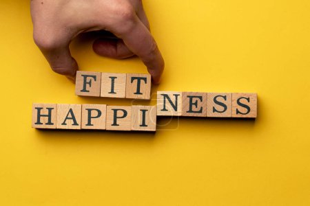 yellow warm background without shadows man hold wooden cubes with black letters laid out word fitness happiness