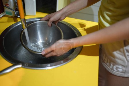 Photo for Washing up a metal bowl under running tap water in a sink - Royalty Free Image