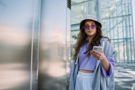 Téléchargez les photos : Cool young girl looking to camera and holding mobile phone. . High quality photo - en image libre de droit