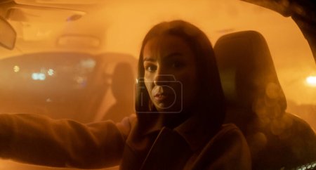 Téléchargez les photos : Portrait de femme sérieuse appréciant la conduite de nuit tout en étant assis dans la voiture et en regardant la caméra. Photo de haute qualité - en image libre de droit