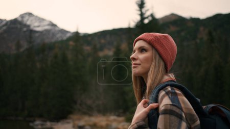 Téléchargez les photos : Portrait view of blonde woman tourist admiring of the mountain views, enjoying fresh air. Girl in hat holding backpack and looking at landscapes - en image libre de droit