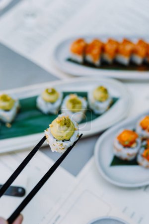 Téléchargez les photos : Vue verticale des mains tenant des sushis wasabi et des rouleaux avec des baguettes en bois dans le restaurant. Concept de cuisine japonaise et chinoise - en image libre de droit