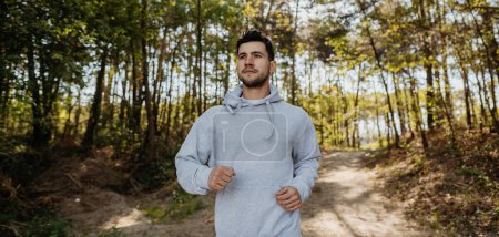 Téléchargez les photos : Portrait de jogging modèle de fitness masculin d'entraînement pour le marathon sur la route forestière dans un paysage naturel étonnant.. Runner homme sprint séance d'entraînement sur route forestière - en image libre de droit