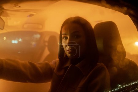 Téléchargez les photos : Portrait d'une femme sérieuse et détendue appréciant la conduite de nuit assis en voiture et regardant la caméra. Patron dame voyageant le soir - en image libre de droit