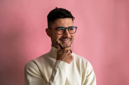 Téléchargez les photos : Portrait d'homme barbu heureux avec des vêtements élégants portant des lunettes riant et regardant à côté de la caméra tout en posant isolé sur fond rose. Concept d'émotions humaines - en image libre de droit
