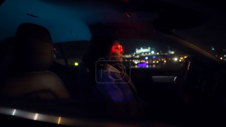 Téléchargez les photos : Jeune belle femme utilise des lunettes de réalité virtuelle dans la voiture pendant la nuit pluvieuse tardive avec vue arrière de la ville lumière au néon - en image libre de droit