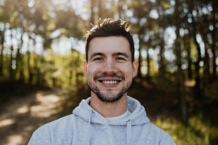 Téléchargez les photos : Homme visage heureux portrait de jeune homme attrayant souriant posant à l'extérieur regardant la caméra dans les bois profiter de la nature - en image libre de droit