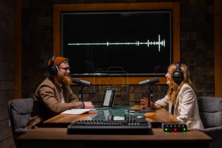 Téléchargez les photos : Deux animateurs de radio parlent et sourient alors qu'ils sont assis près des microphones dans un studio de radiodiffusion. Concept d'occupation créative - en image libre de droit