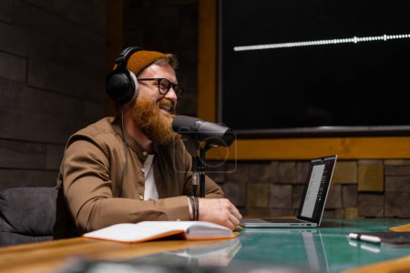 Téléchargez les photos : Animateur de radio souriant et gestuel avec écouteurs lisant les nouvelles dans le microphone studio à la station de radio avec des lumières - en image libre de droit