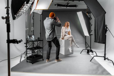Téléchargez les photos : Un homme capture une femme posant sur un cube dans un studio photo, célébrant un événement avec du matériel photo professionnel et des accessoires de studio - en image libre de droit