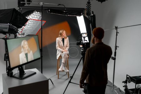 Téléchargez les photos : Un homme capture une femme sur un tabouret dans un studio, en utilisant du matériel scénique et audio pour créer un - en image libre de droit