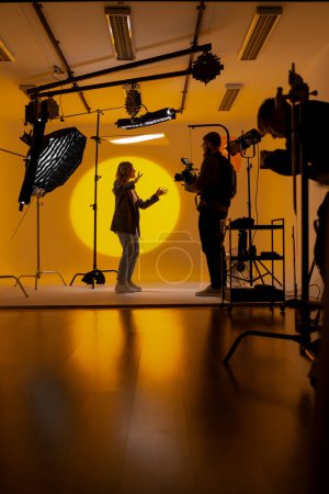 Téléchargez les photos : Un vidéaste capte des images dans une pièce jaune à l'aide d'une caméra vidéo, mettant en valeur son talent dans l'industrie cinématographique en tant que cinéaste - en image libre de droit
