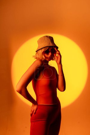 Photo for Fashionable portrait of blonde lady in sunglasses posing isolated on orange background. Lady in trendy jacket outfit gesturing hands to camera - Royalty Free Image
