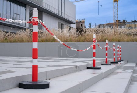 Photo for Bright orange traffic cones and plastic chain or car barriers. Side view of orange plastic street cones and poles with reflective silver tape near chain link fence at the entrance of a building. - Royalty Free Image