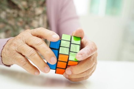 Téléchargez les photos : Bangkok, Thaïlande - 15 mai 2022 Femme âgée asiatique jouant au jeu Rubik cube pour pratiquer la formation du cerveau pour aider la prévention de la démence et la maladie d'Alzheimer. - en image libre de droit